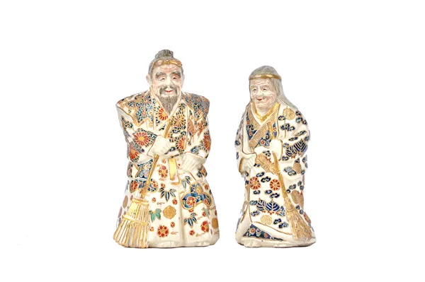 A pair of Japanese Satsuma figures of an elderly man and a woman, second half 19th century, each modelled standing in long robes with a broom,  the wo