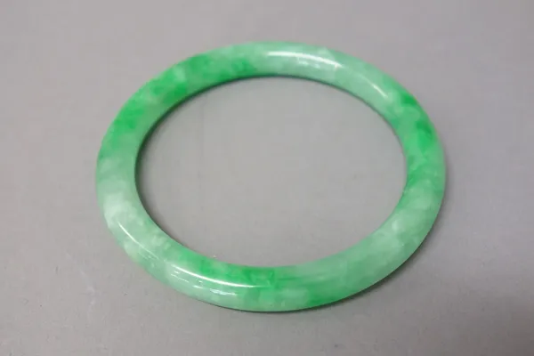 A Chinese jadeite bangle, of apple green and grey tone, 7.5cm. diameter.