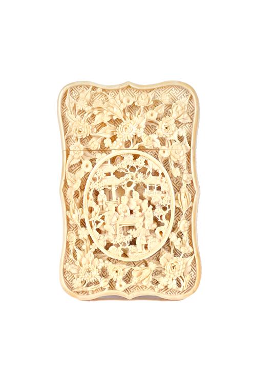 A Canton ivory card case, late 19th century, of shaped rectangular form, carved with a panel of figures seated around a table inside an oval frame aga