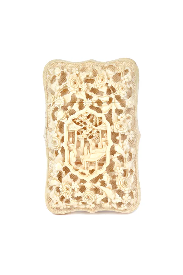 A Canton ivory rectangular card case, late 19th century, of shaped rectangular form, carved with a panel of figures at a table inside a barbed frame a