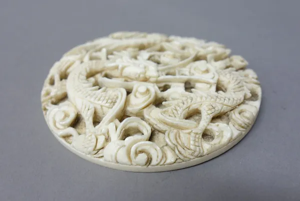 A Chinese ivory circular plaque, late 19th/early 20th century, carved with a dragon amongst cloud scrolls, 7cm. diameter.