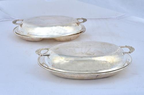 Two similar oval lidded entree dishes, one having a twin compartment to the base, detailed Silver, the other with a plain oval base, detailed Silver,