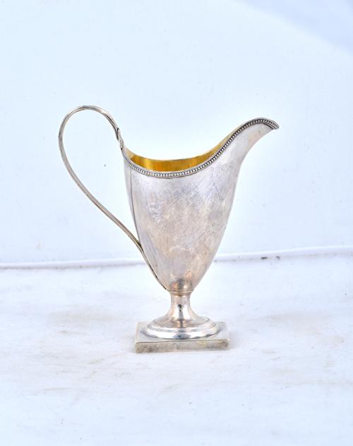 A George III silver cream jug, of helmet shaped form, decorated with a beaded rim and raised on a square foot, crest engraved, maker possibly John Lam