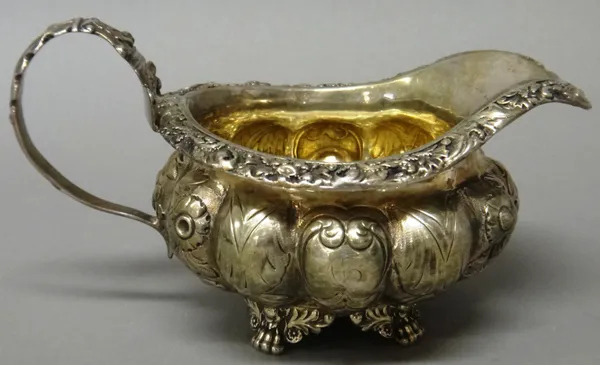 A George IV silver milk jug, of compressed lobed circular form, with embossed decoration, within a wide cast rim, raised on four feet, London 1827, we