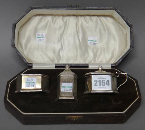 A silver three piece condiment set, comprising; a salt, a pepperette and a mustard pot, each piece of angular form, having a decorated rim, Birmingham