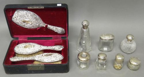 A silver mounted three piece brush and mirror set, comprising; a pair of hairbrushes and a hand mirror, each piece with floral and scroll embossed dec