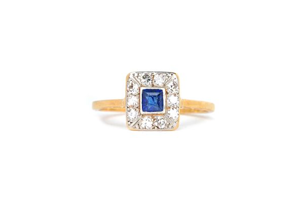 A gold and platinum, sapphire and diamond rectangular cluster ring, claw set with the emerald cut sapphire at the centre, in a surround of ten circula