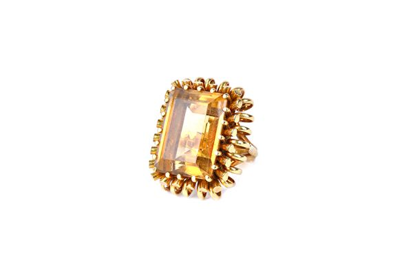 A gold and citrine single stone ring, claw set with a large rectangular step cut citrine, within a looped wirework surround, between split shoulders,