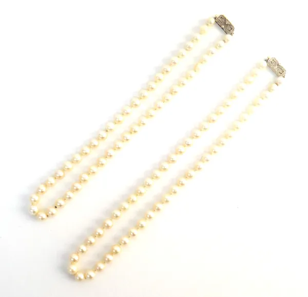 Two single row necklaces of uniform cultured pearls, each on a gold and diamond set clasp, in a cut cornered rectangular design, one detailed 14 K, le