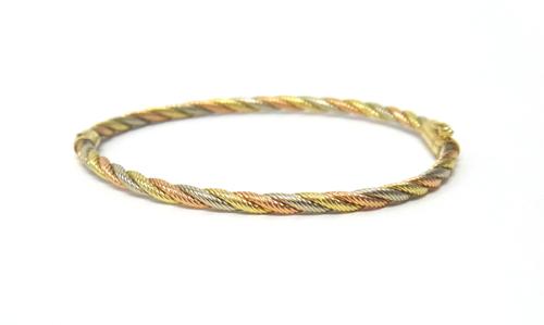 A three colour gold oval hinged bangle, in a ropetwist design, on a snap clasp, with a foldover safety catch, detailed 14 K, weight 6.2 gms.