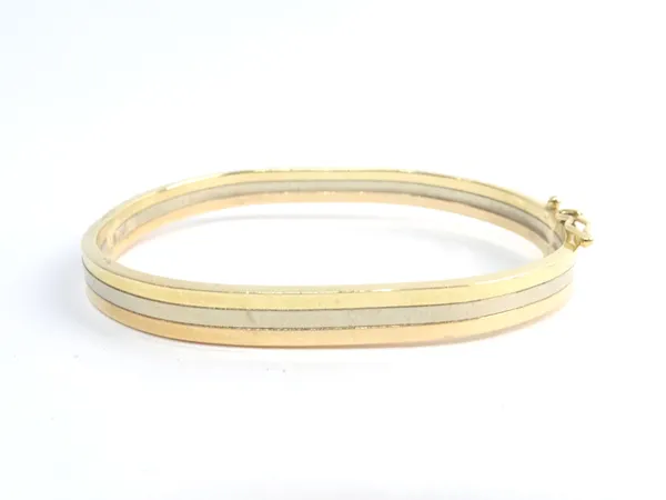 A three colour gold oval hinged bangle, on a snap clasp, with a foldover safety catch, gross weight 8.7 gms.