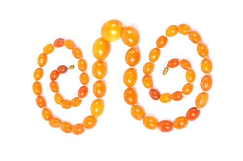 A single row necklace of graduated oval varicoloured butterscotch coloured amber beads, on a base metal clasp, gross weight 105 gms. Illustrated