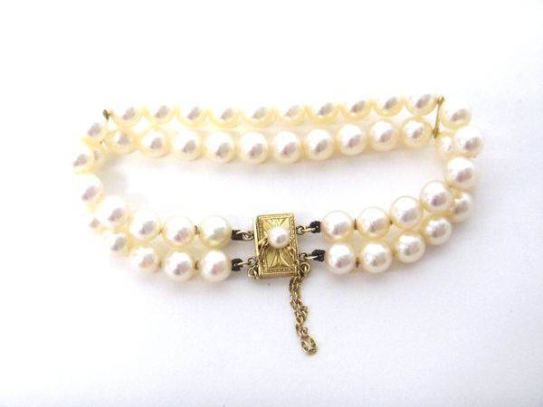 A two row bracelet of uniform cultured pearls, on a rectangular gold clasp, mounted with a cultured pearl, detailed K 14, fitted with a safety chain.