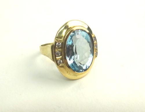 A gold, blue topaz and diamond ring, mounted with the oval cut blue topaz to the centre, between diamond set three stone sides, mounted with circular