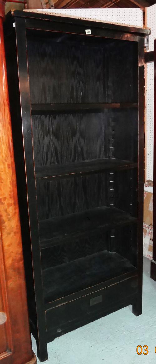 LOMBOK; A 20th century black painted hardwood open floor standing bookcase of tapering form, with single drawer to base, 80cm wide x 190cm high. L7