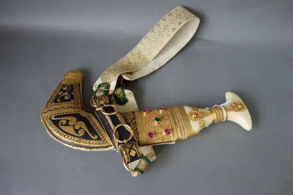 A late 20th century jambia, ornately decorated with gilt metal, housed in a leather scabbard.