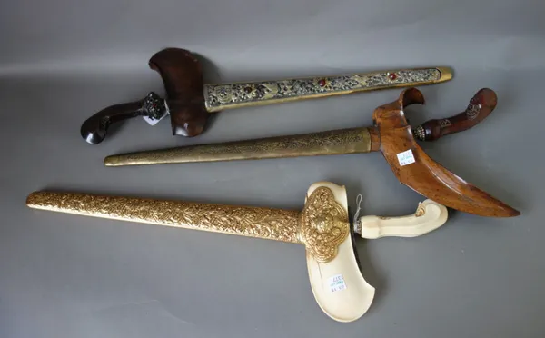Three 20th century Sumatran kris, two with carved wooden handles, each with a metal bound wooden scabbard, (3).