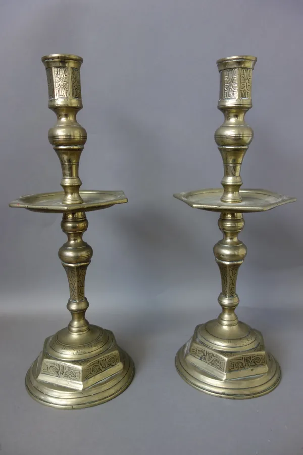 A pair of heavy brass candlesticks, possibly 18th century, with large hexagonal drip pan and a circular turned base, with all over foliate decoration,