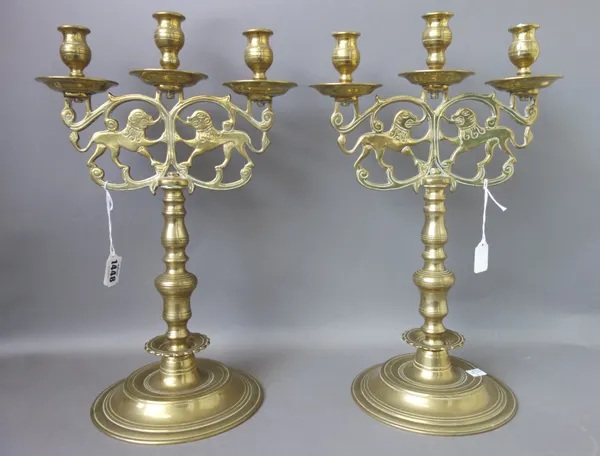 A pair of North European three branch brass candelabra, 19th century, cast with opposing tigers over a turned stem and circular foot, 42cm high, (2).