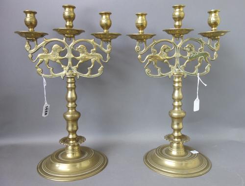 A pair of North European three branch brass candelabra, 19th century, cast with opposing tigers over a turned stem and circular foot, 42cm high, (2).