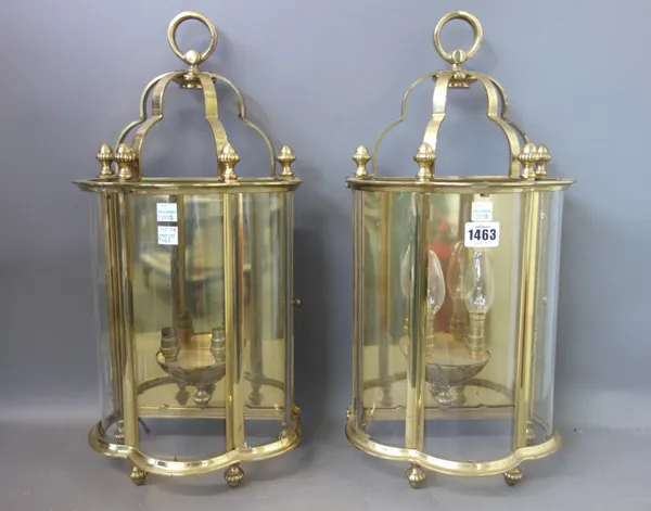 A pair of modern brass and glass wall lights, each with three shaped glass panels enclosing a two branch light fitment surmounted with a loop handle,