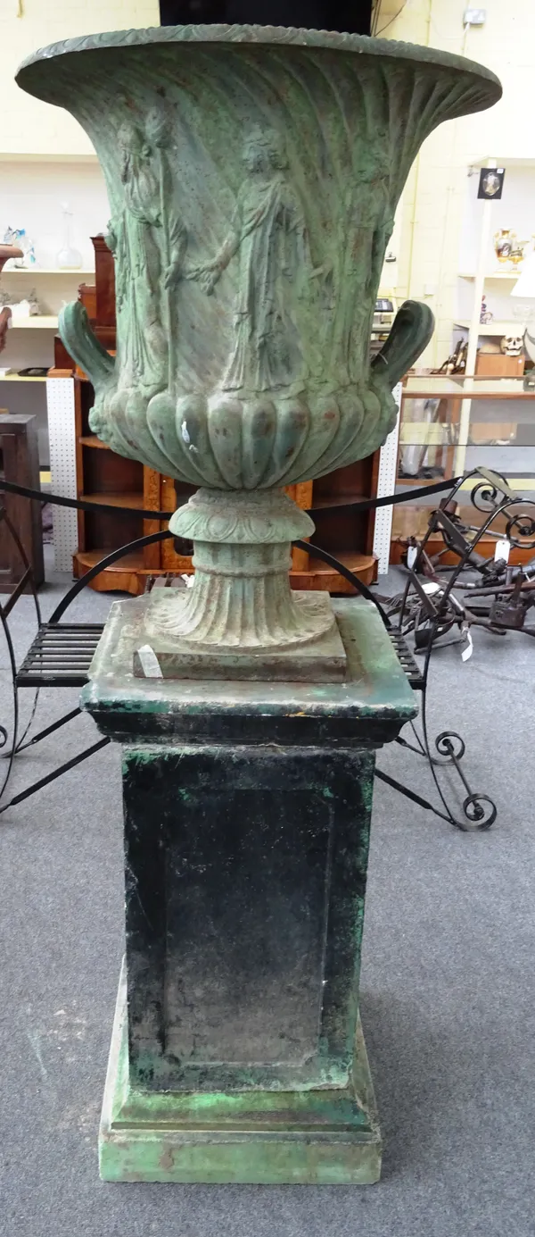 A cast iron faux bronze patinated garden urn, relief cast with classical figures on a reconstituted stone stepped square pedestal, the urn 65cm diamet