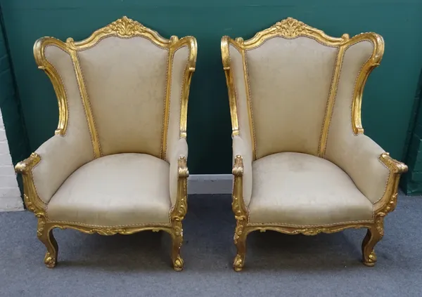 A pair of 18th century style gilt framed wingback armchairs, with shell carved crest and serpentine seat on scroll supports, 83cm wide x 118cm high.