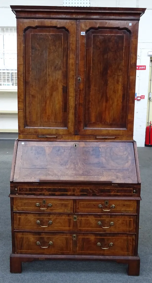 An early 18th century feather banded figured walnut bureau cabinet, the pair of shaped panelled doors over a pair of candle slides with stepped and we