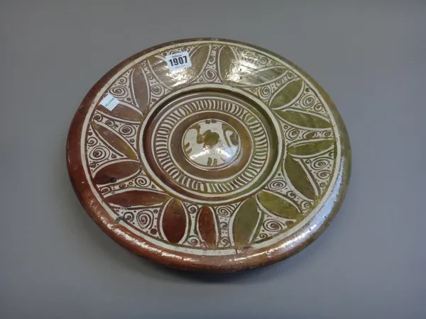 An Hispano Moresque copper lustre dish, 16th century, with central raised boss beneath a border of leaves and scrolls, (a.f), 31 cm. diameter.