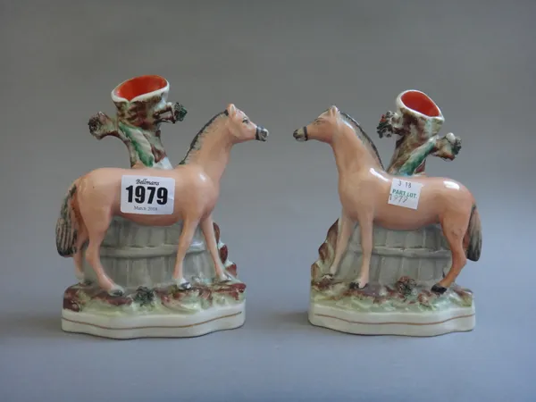 A pair of Staffordshire pottery spill vases, mid 19th century, each modelled as a pony standing against a fence and tree, on a shaped oval grassy base