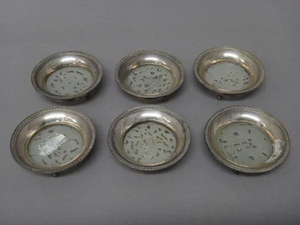 Six Japanese circular dishes, each base glazed with a carved and pierced pale green stone panel, within decorated rims and raised on three spherical f