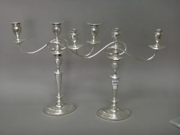 A pair of plated three light table candelabra, each having fluted scrolling arms and raised on an oval base, in the early 19th century taste (three sc