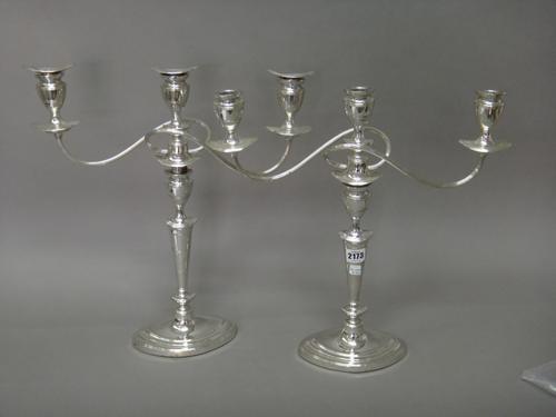 A pair of plated three light table candelabra, each having fluted scrolling arms and raised on an oval base, in the early 19th century taste (three sc