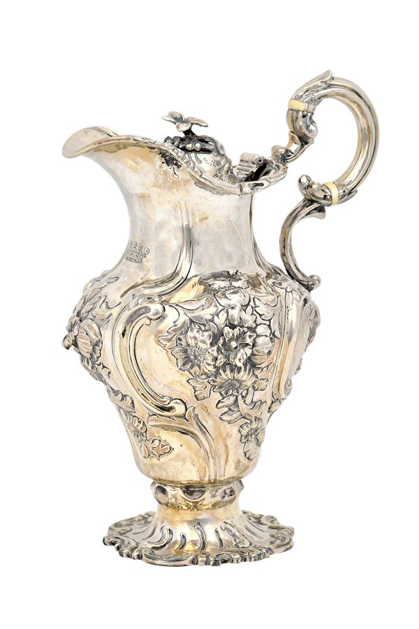 A Victorian silver hinge lidded small hot water jug, the body embossed with floral panels within scrolls, with an insulated scrolling handle, the hing