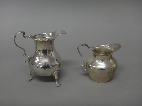 A George III silver milk jug, of baluster form, having a shaped rim and raised on three feet, London probably 1764 and a late Victorian silver milk ju