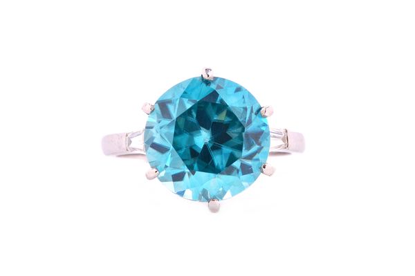 A blue zircon and diamond ring, claw set with the circular cut blue zircon at the centre between tapering baguette diamond single stone shoulders, rin