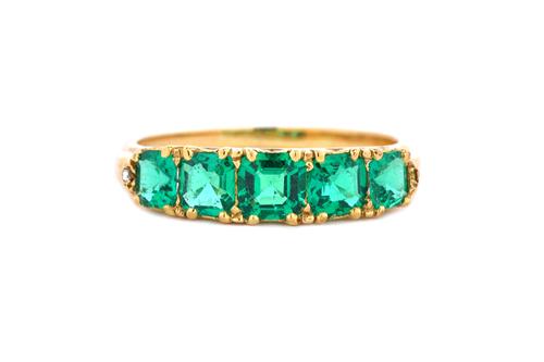 A gold and emerald set five stone ring, mounted with a row of graduated step cut emeralds, the mount decorated with pierced sides, the emeralds weigh