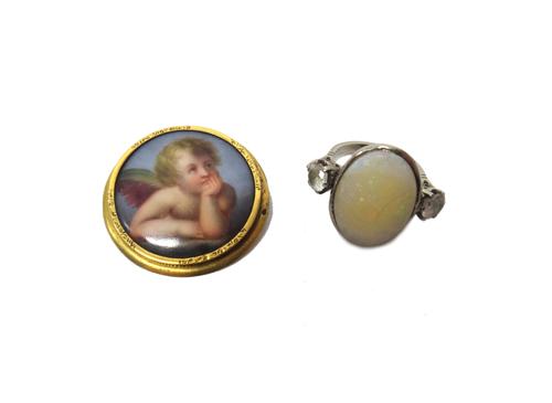 A gold mounted circular ceramic brooch, designed as the portrait of a pensive cherub, backed with mother of pearl and an opal and colourless gem set t