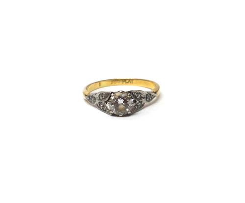 A gold and platinum, diamond set ring, claw set with the principal circular cut diamond at the centre, between diamond set three stone foliate shoulde