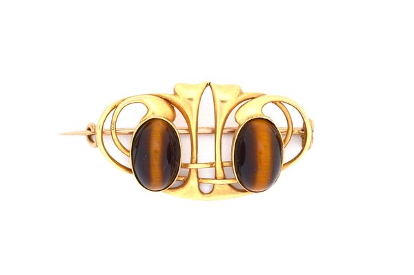 A gold and tiger's eye brooch, in a curved and pierced Art Nouveau inspired design, mounted with two oval cabochon tiger's eyes.  Illustrated