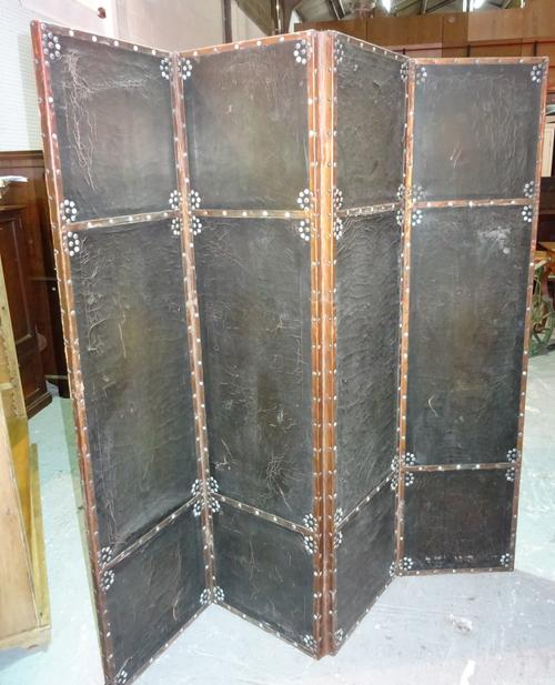 An early 20th century stained pine and black leather four fold screen with studded decoration, 164cm wide x 168cm high.  G10