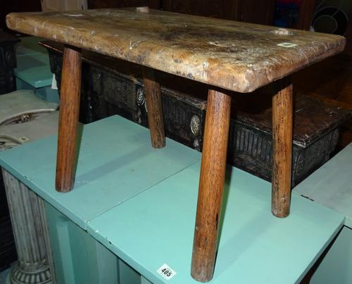 An early 19th century primitive stool, with elm top and ash stake supports, 53cm wide x 40cm high.  M6