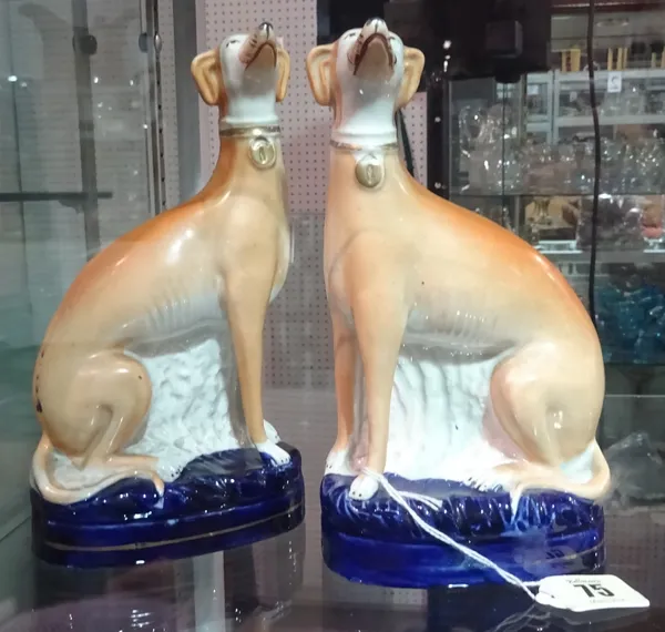 A pair of Staffordshire pottery models of seated greyhounds, mid-19th century, each wearing a gilt collar, on an oval blue washed base, 19.5cm high, (