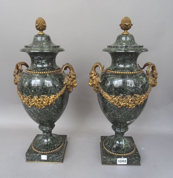A pair of early 20th century French ormolu mounted verde antico marble vases, in the Louis XVI style, with pineapple finials above stylized rams head