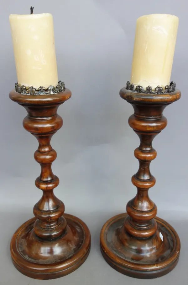 A pair of Continental fruitwood candlesticks, of turned circular form, on dished bases, with gilt metal castellated sconces and candles, the candlesti