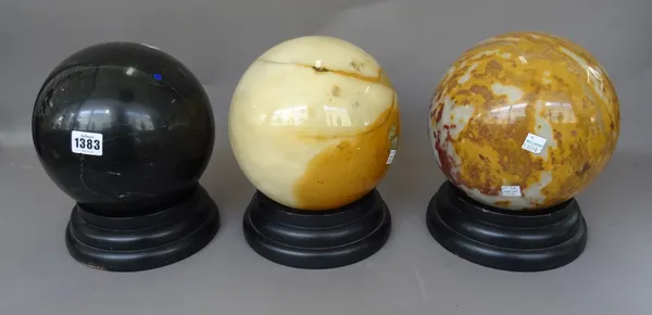 Three hardstone spheres on ebonised wooden stands, 20th century, one smaller, and a clear glass sphere on a wooden stand, the largest 19cm diameter, (