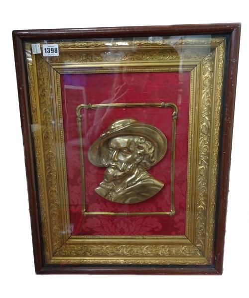 A Victorian style gilt metal half block plaque, depicting a bust of a King Charles Cavalier, against a foliate crimson textile ground, within a giltwo