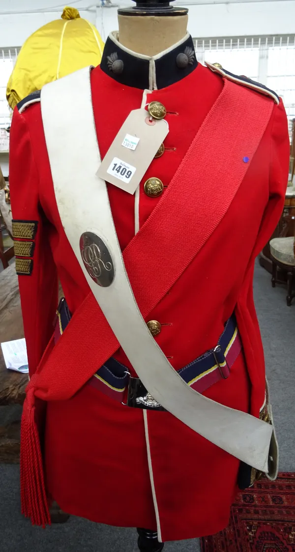 A British military officer's red tunic, sash and belt displayed on an ebonised wood and shaped tailor's dummy by Siegel Stockman, London.