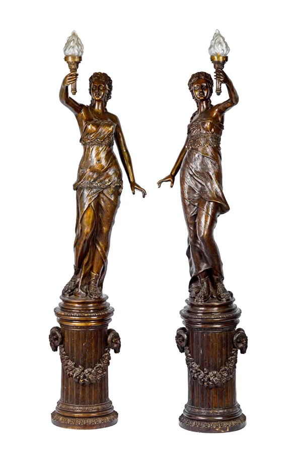 A pair of modern patinated bronze figures, each modelled and cast as a female Romanesque torch bearer, one hand raised with a frosted shade, each on a