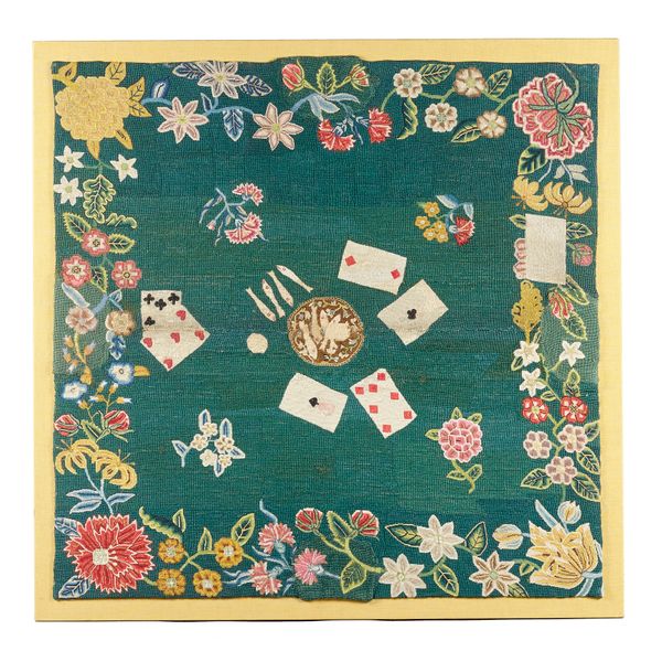 A George II needlework card table cover, on a green ground, the centre woven with cards and 'fish' within a foliate border in polychrome colours, with
